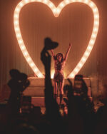 Sabrina Carpenter on stage in front of large neon heart